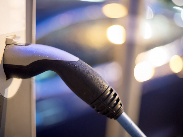 Electric car recharging with charge cable and plug leading to charge point. Night.